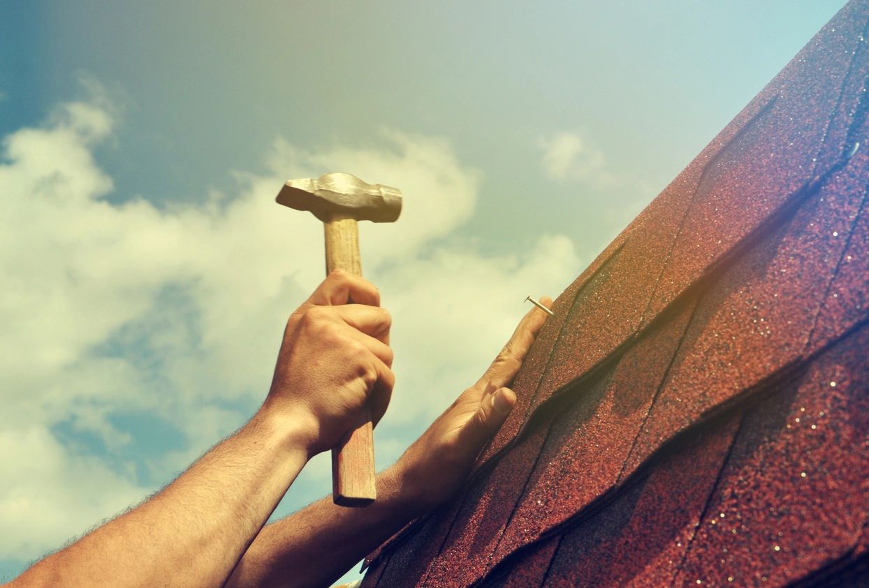 A person holding a hammer on top of a roof.