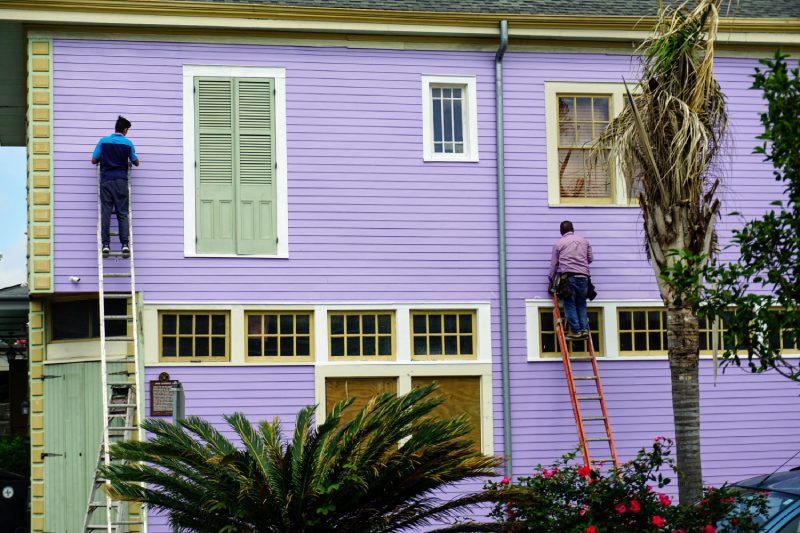 A man on a ladder painting the outside of a house.